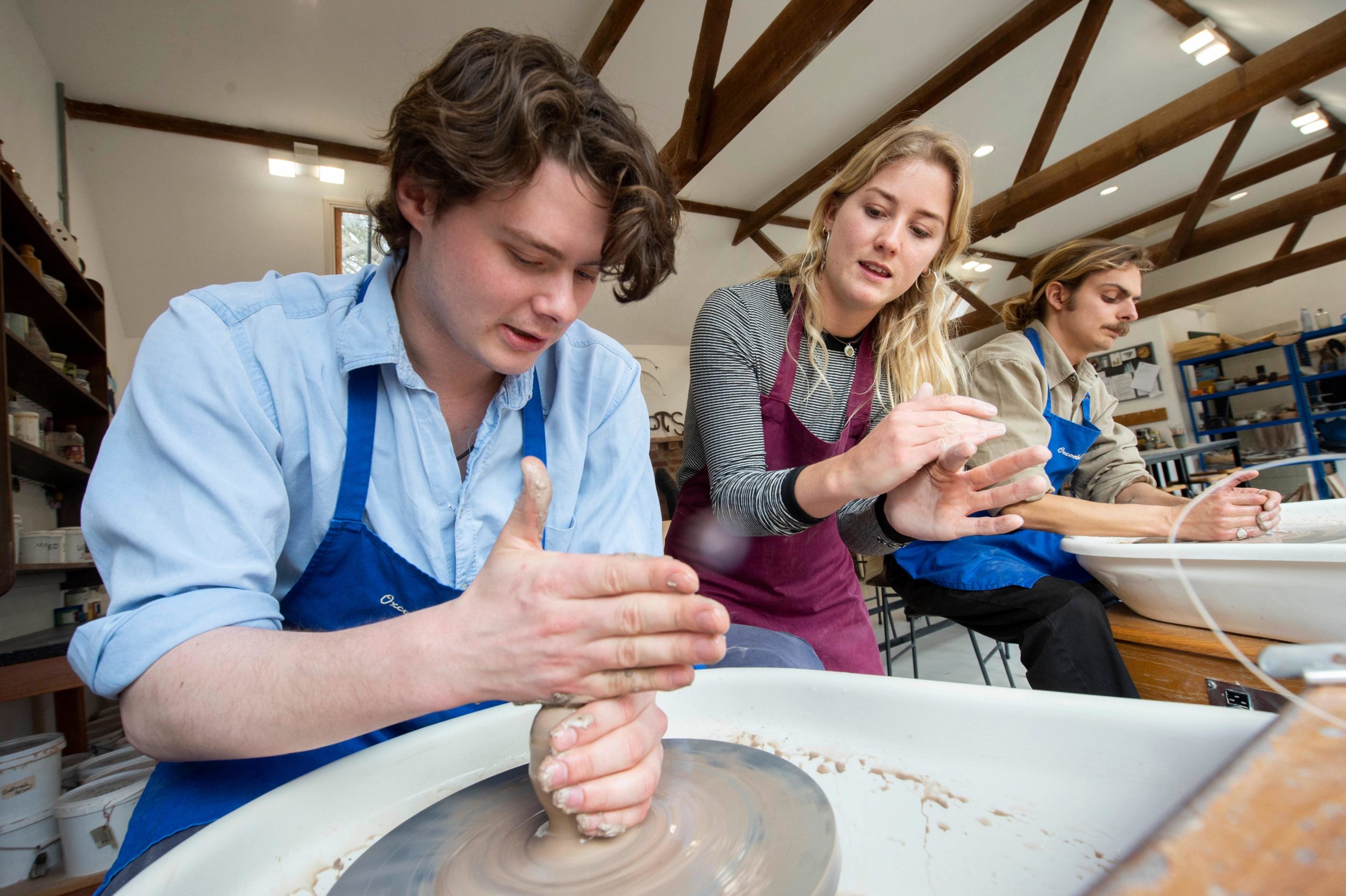 Two people being guided using the pottery wheels